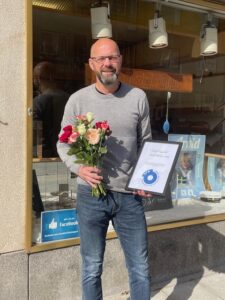 Tomas Yngström glatt leende med blommor och ett diplom från FFS i sin hand.